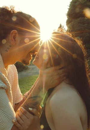 A romantic sunlit moment captured outdoors with golden sun rays creating lens flares through trees.