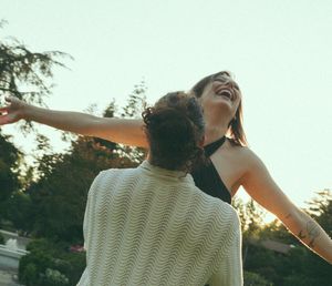A person dances in a white knit sweater against a sunset backdrop, with their arms expressively raised in motion.