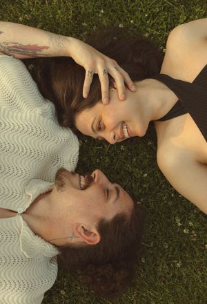 Two people lying on grass wearing white and black clothing while enjoying a carefree moment together.