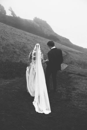 A couple in wedding attire walking up a mountainside slope in dramatic black and white photography.