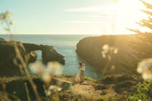 Scenic coastal cliffs at sunset with ocean views and silhouetted figure standing on rocky overlook.