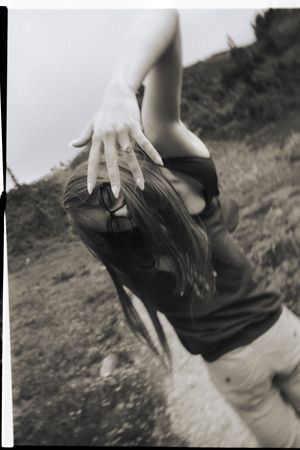 Black and white photo of a woman bending forward with long nails visible, set against a natural outdoor background.