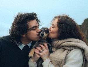 Couple kissing small dog together while wrapped in cozy winter wear.