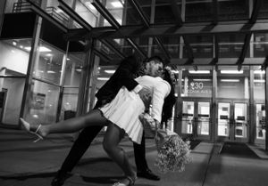 Dramatic black and white nighttime couple portrait outside illuminated building.