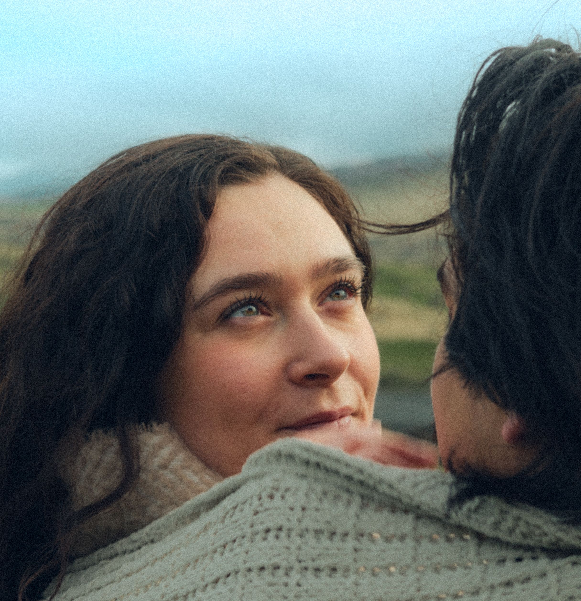 Close-up intimate moment between couple wrapped in knit sweater outdoors.