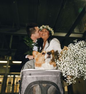 Happy couple with floral crown and dog in pet carrier surrounded by baby's breath flowers.