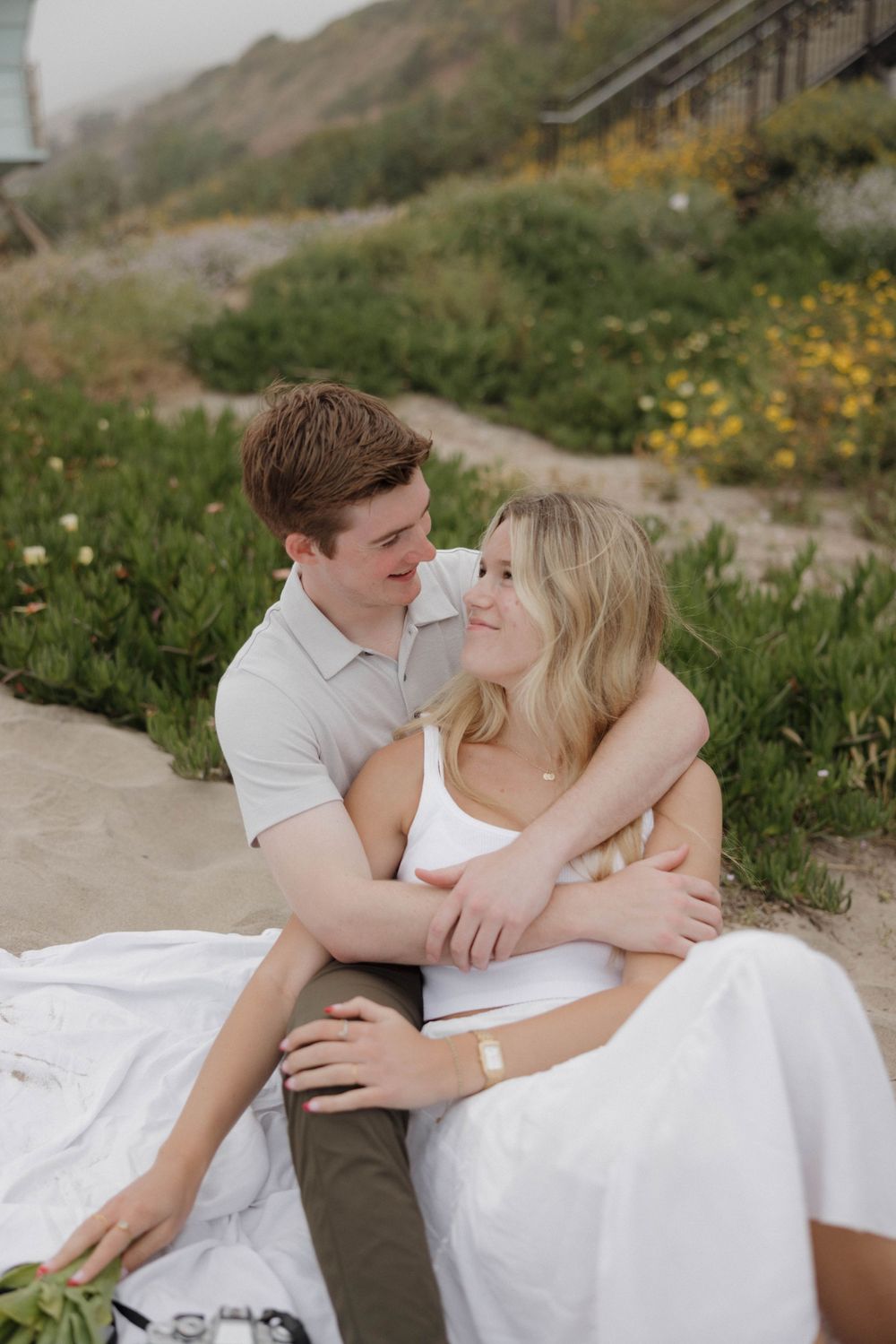 Intimate moment captured during coastal photoshoot with couple on white blanket.