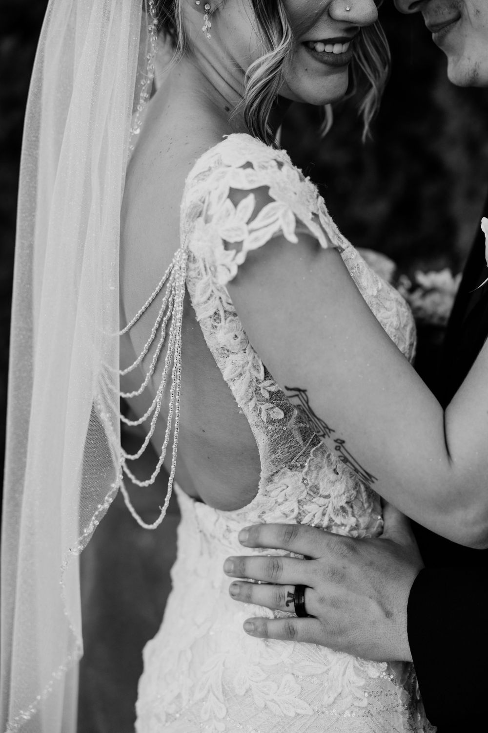 Black and white wedding photo showing intricate lace dress details with draped pearl strands and a delicate veil.