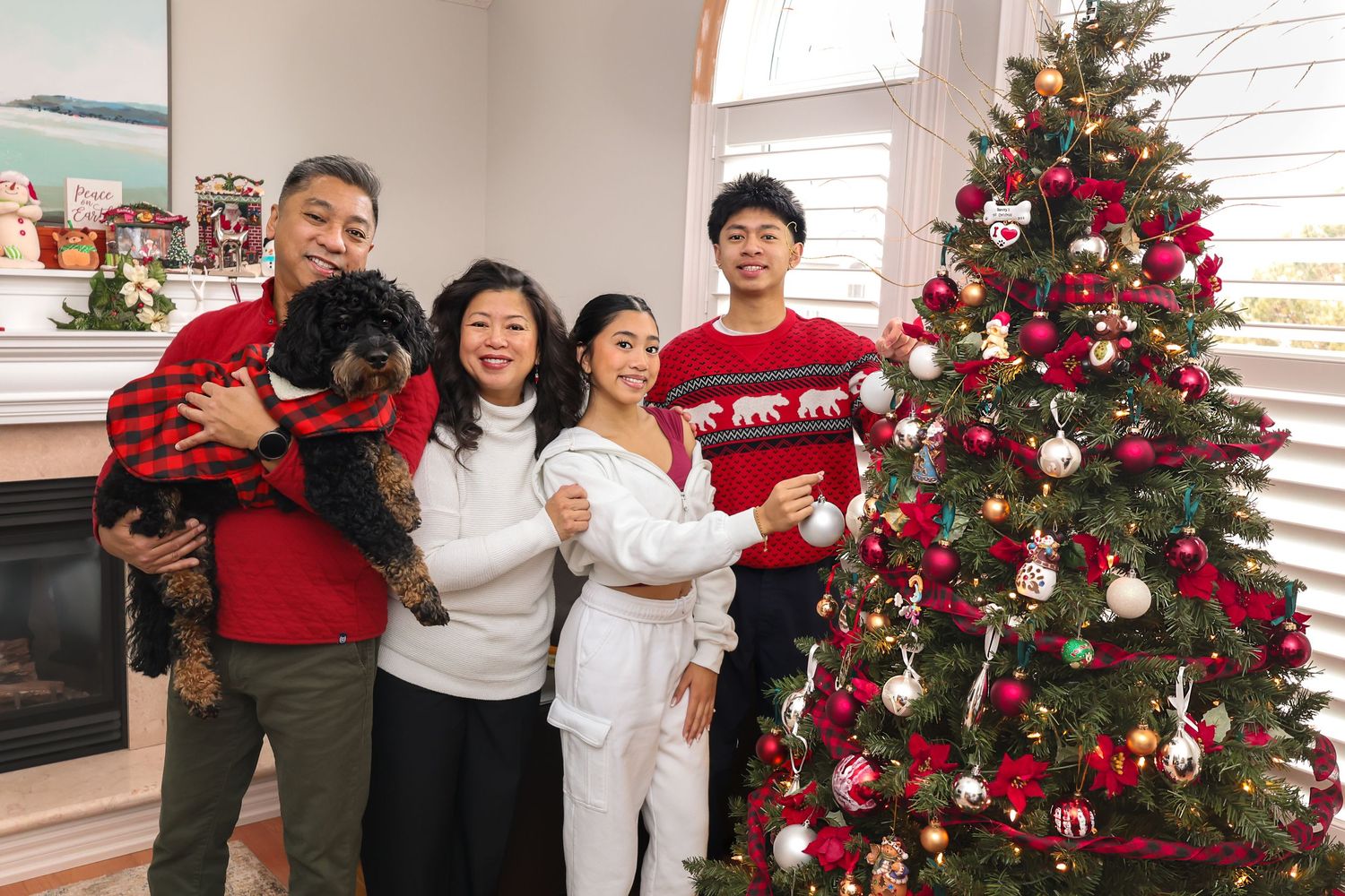 Family around a Christmas tree and fireplace with their family dog, posing for a photo