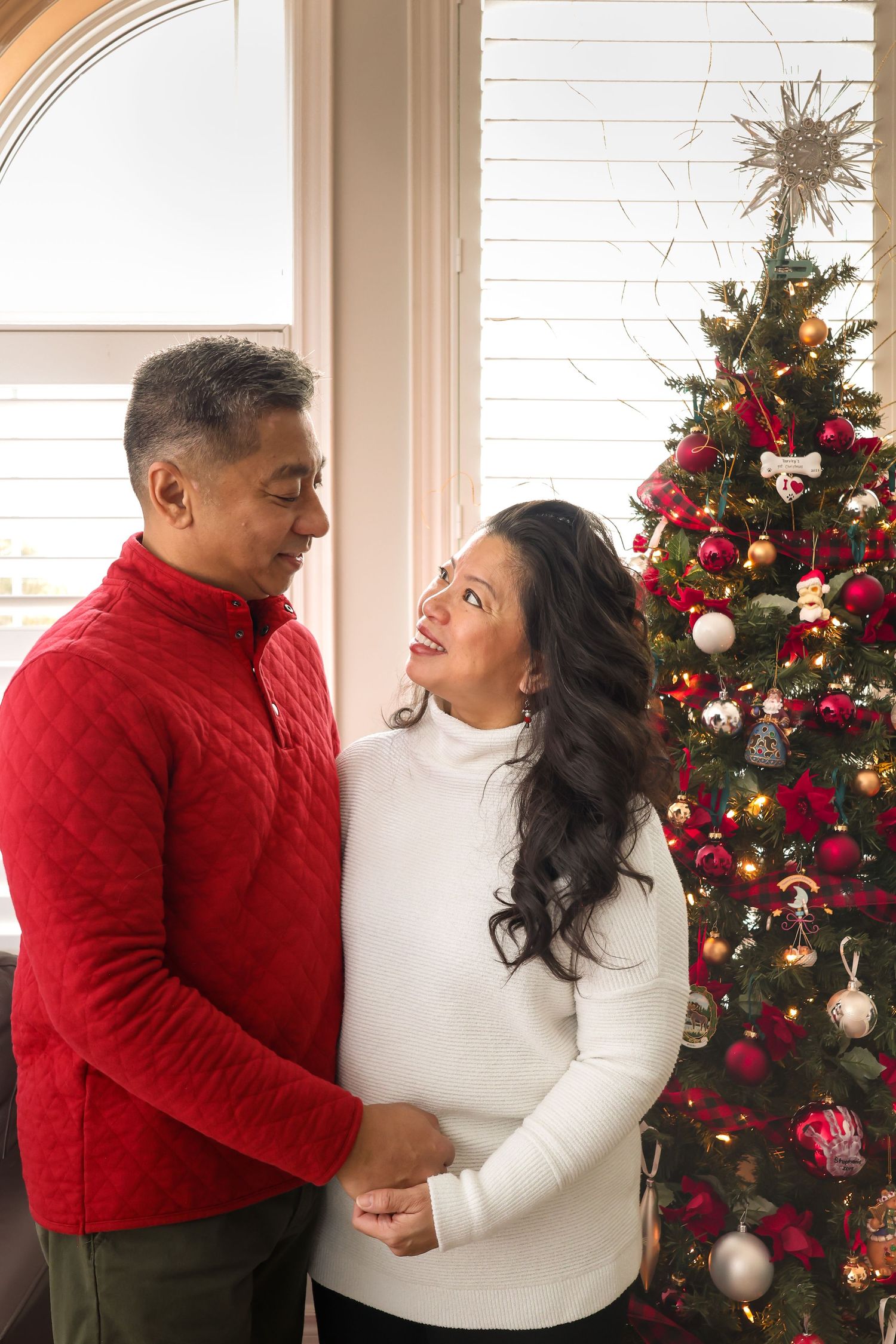 A couple staring at each other lovingly next to their Christmas tree