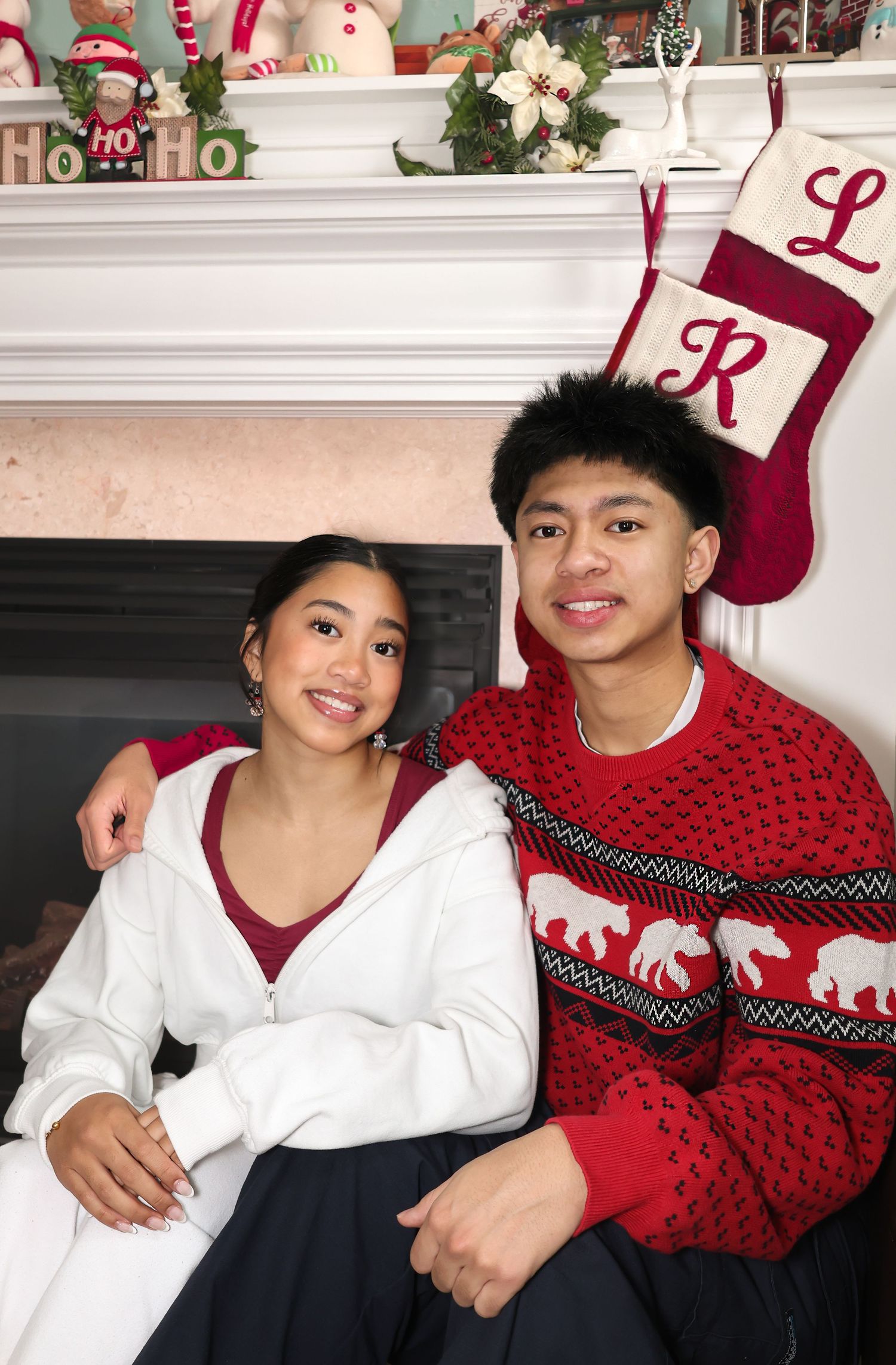 Siblings posing for a Christmas photo next to a fireplace