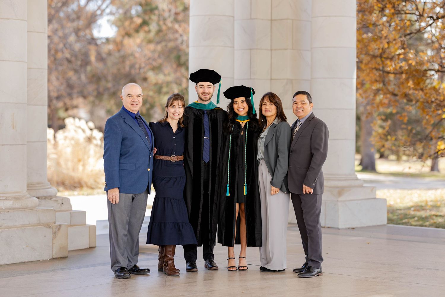 A graduation ceremony photo with family members standing between classical columns in autumn.