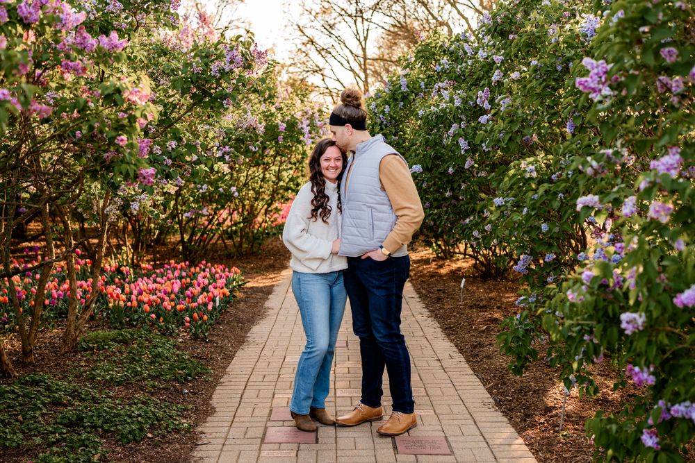 Two people stand close together on a garden path surrounded by blooming pink flowers during golden hour.