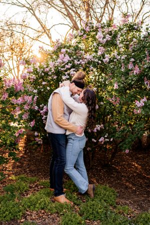 A couple shares a romantic moment beneath blooming pink flowers in a garden at sunset.