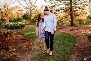 A couple walks hand in hand along a garden path during golden hour as spring flowers bloom nearby.