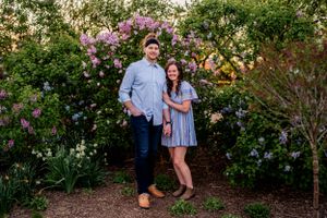 A couple stands together in a garden with beautiful blooming pink crape myrtle trees in the background.