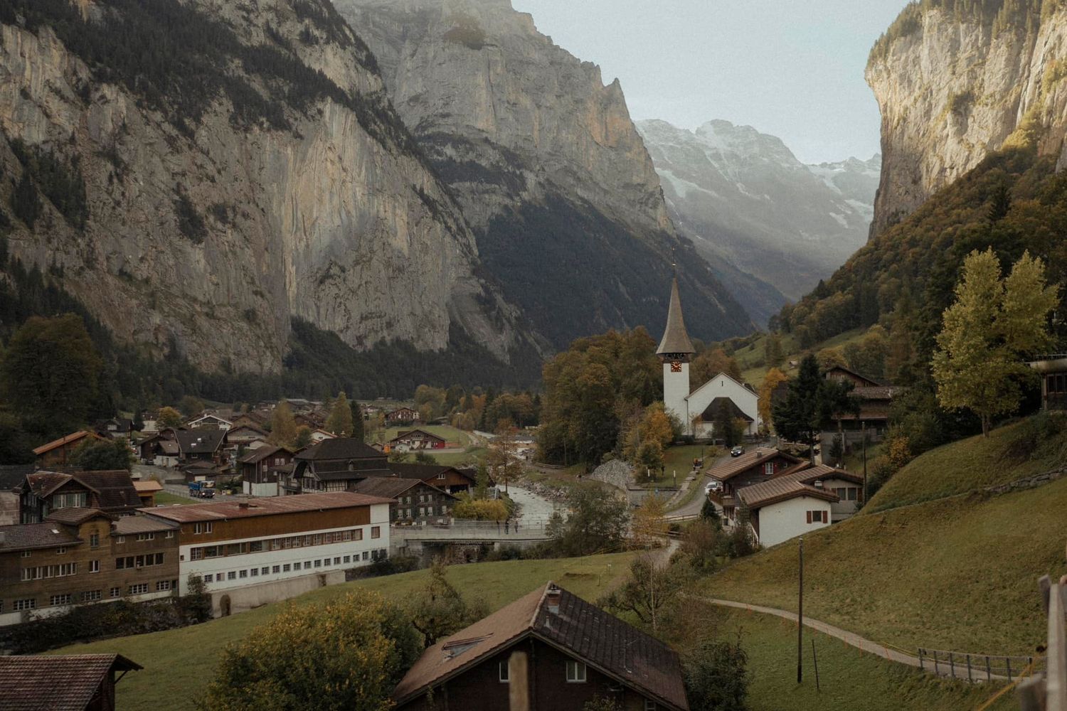 Picturesque Swiss village with white church nestled in valley between dramatic mountain peaks.