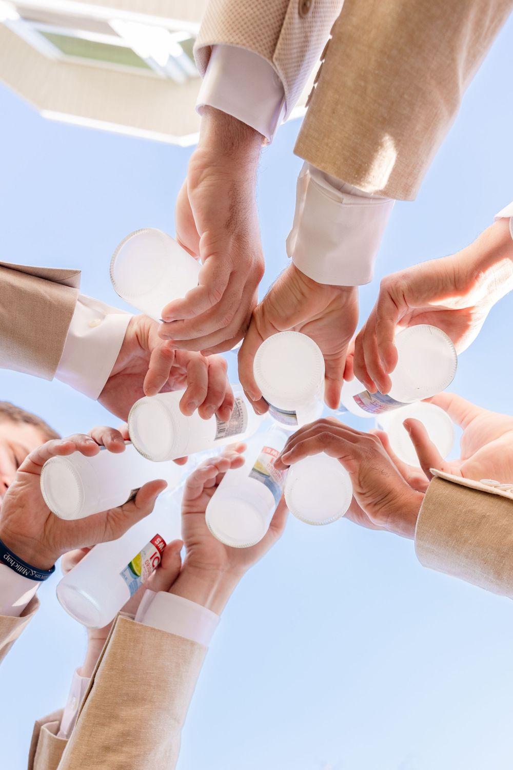 Group of people toasting with white paper cups against a blue sky, viewed from below.