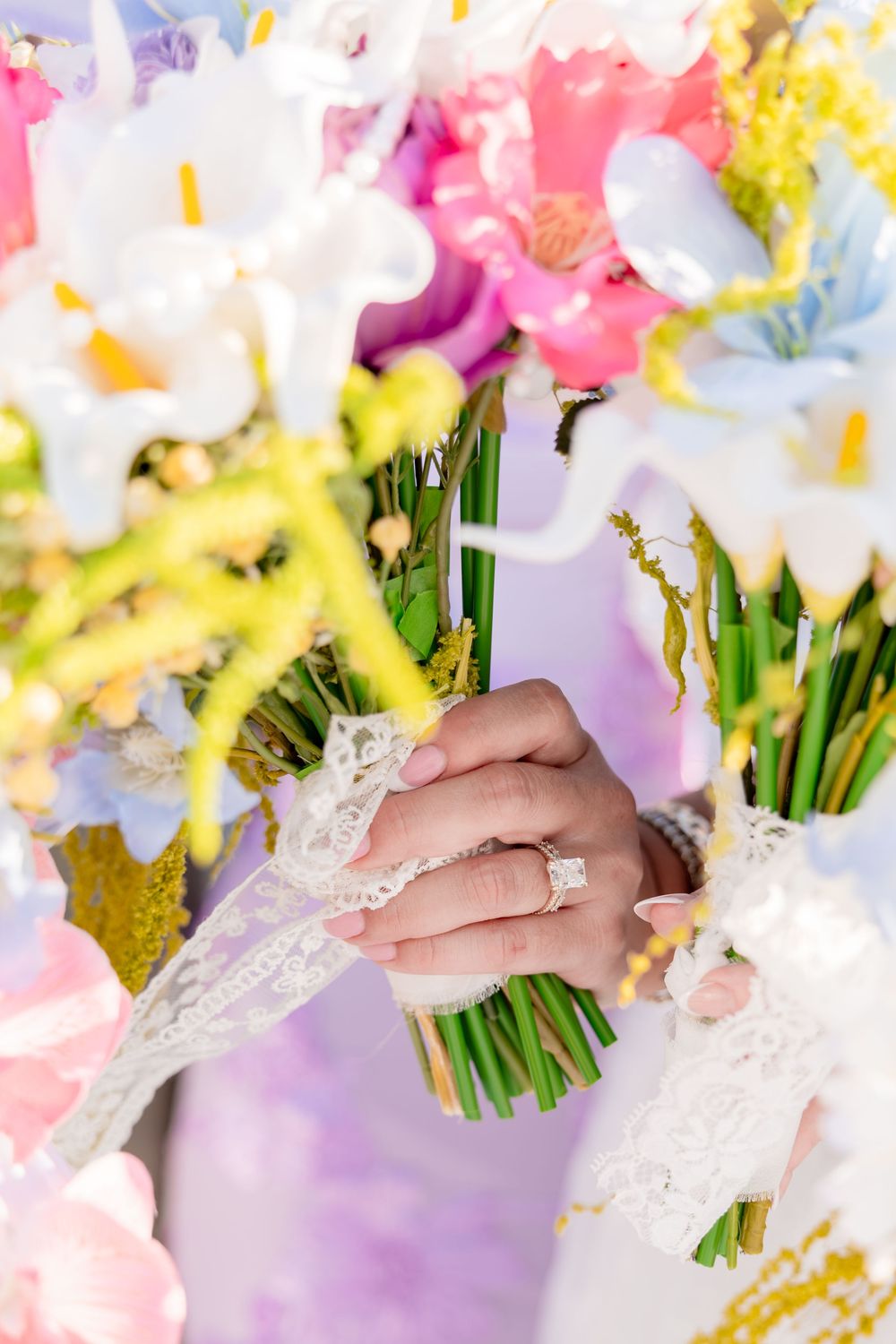 Bride holding colorful spring wedding bouquet with white orchids and pink flowers, wearing lace glove and diamond engagement ring.