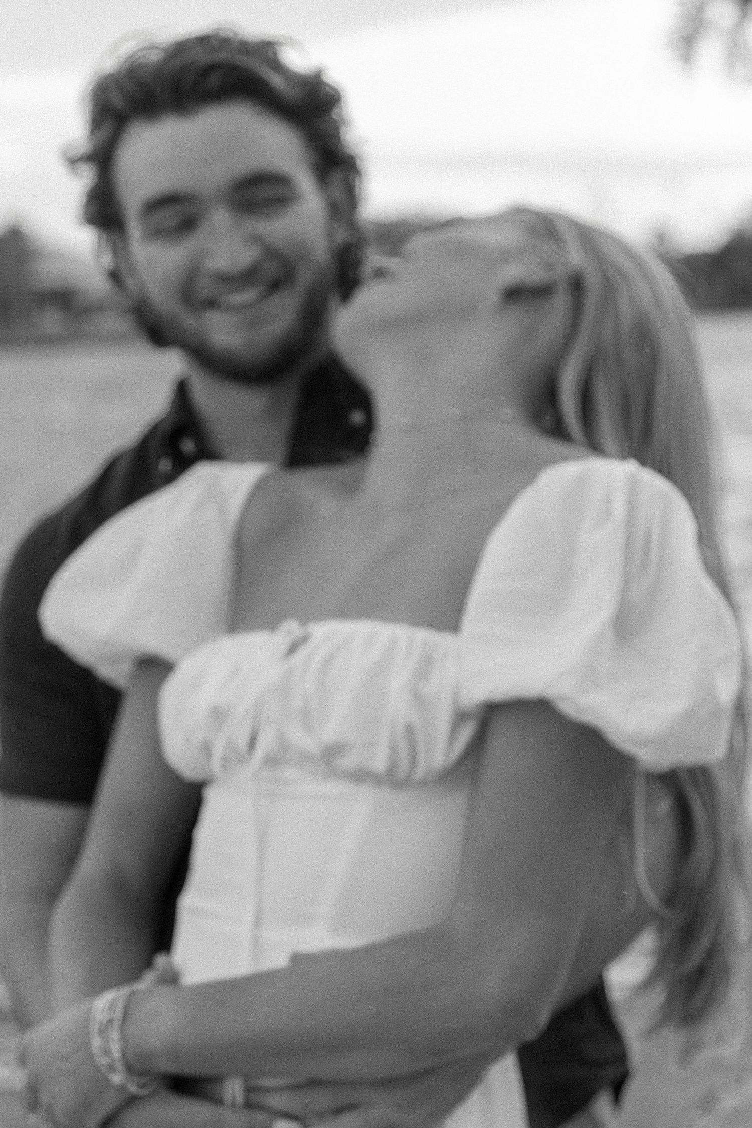 Black and white photo of a smiling couple embracing outdoors in a romantic moment.