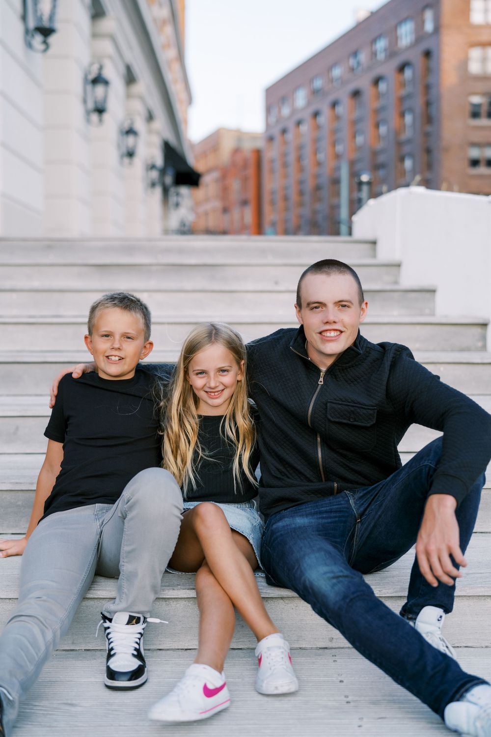 Group sitting together on concrete steps in casual attire against urban backdrop.