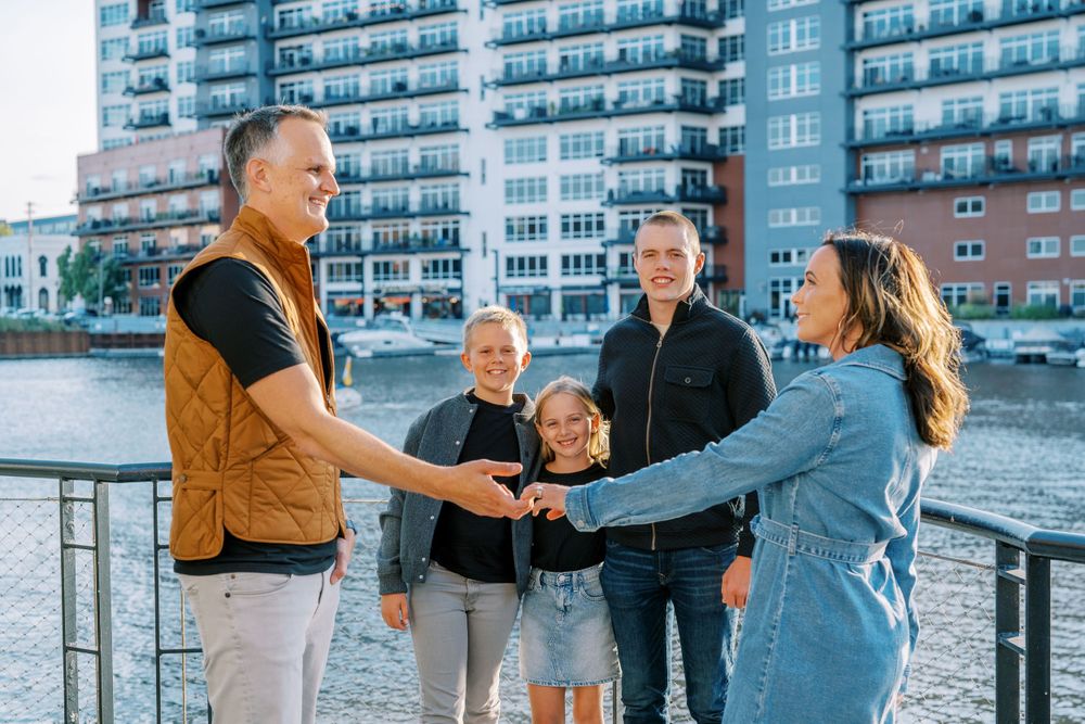 Urban family photoshoot on waterfront boardwalk with apartment buildings in background.