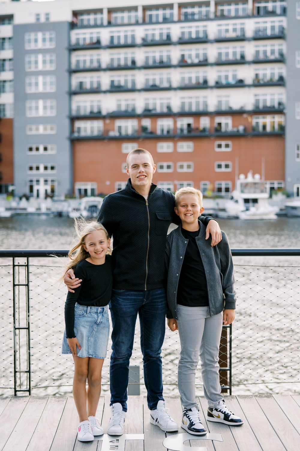 Family members posed casually on wooden dock with waterfront apartments behind them.