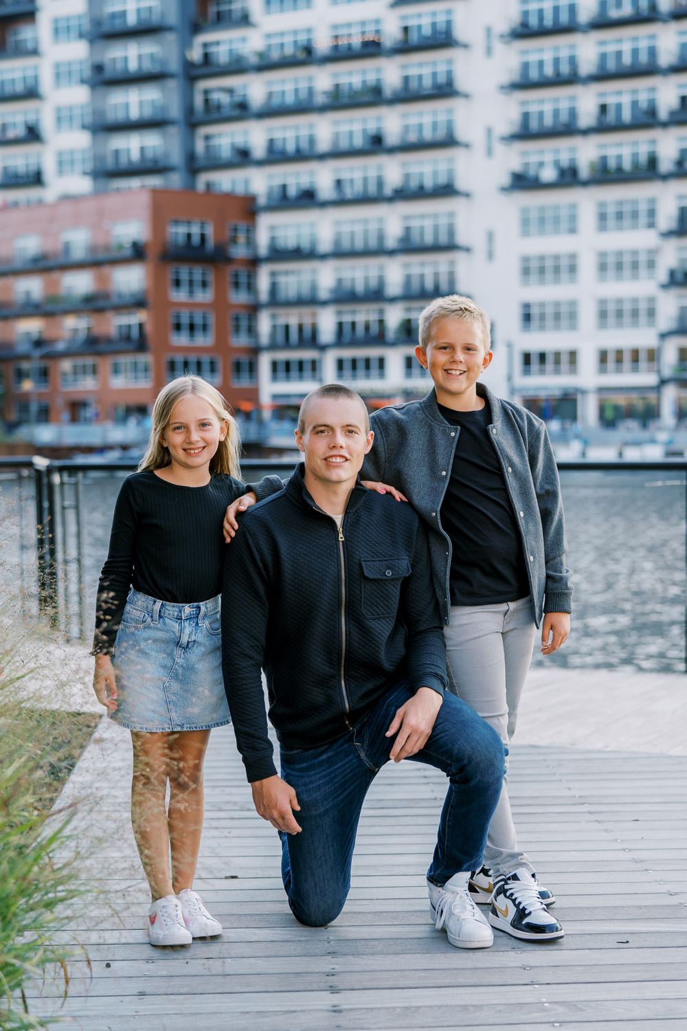 Family members kneeling together on a wooden boardwalk with apartment buildings in the background.