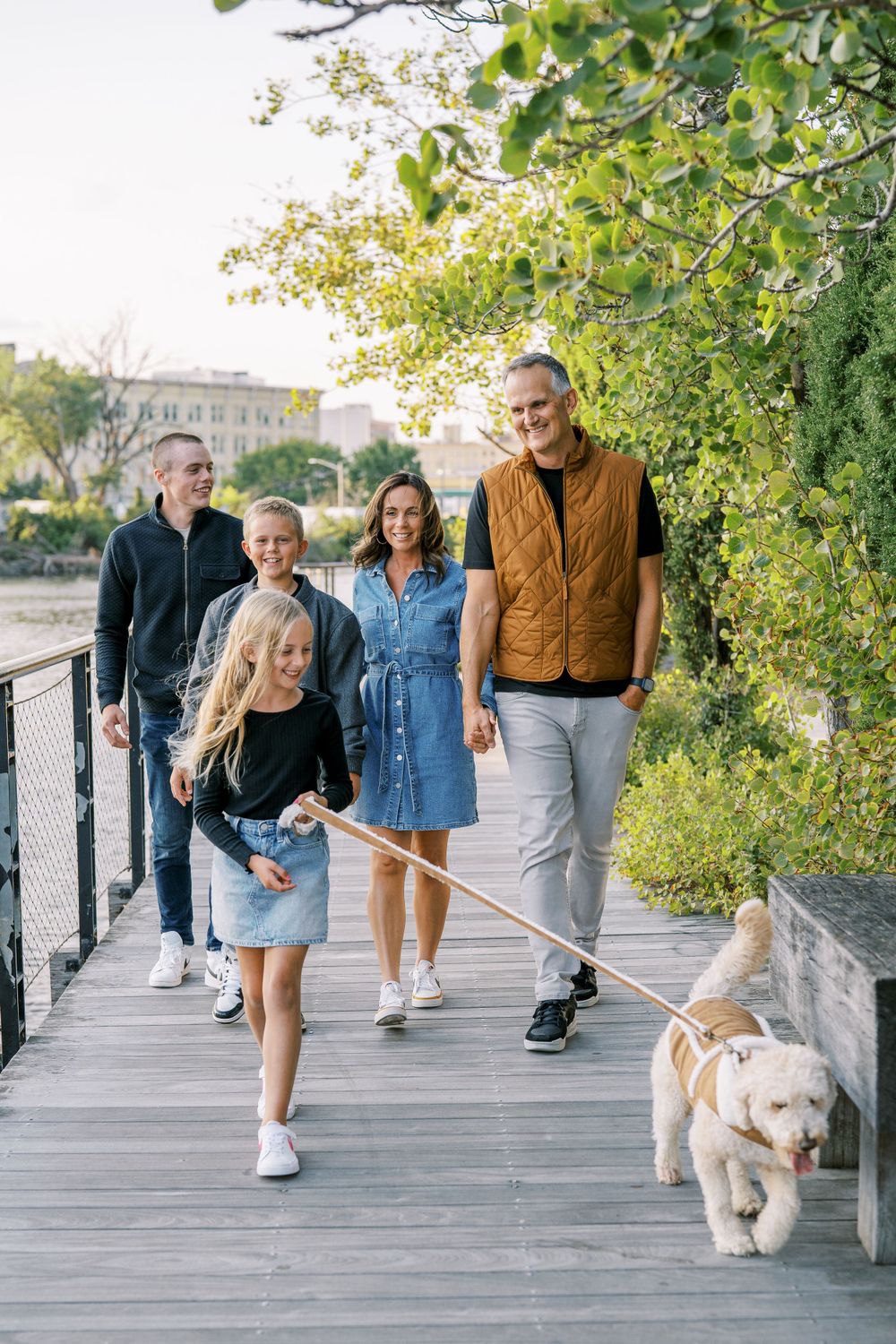 Group taking a leisurely walk with their dog on a sunny boardwalk path.