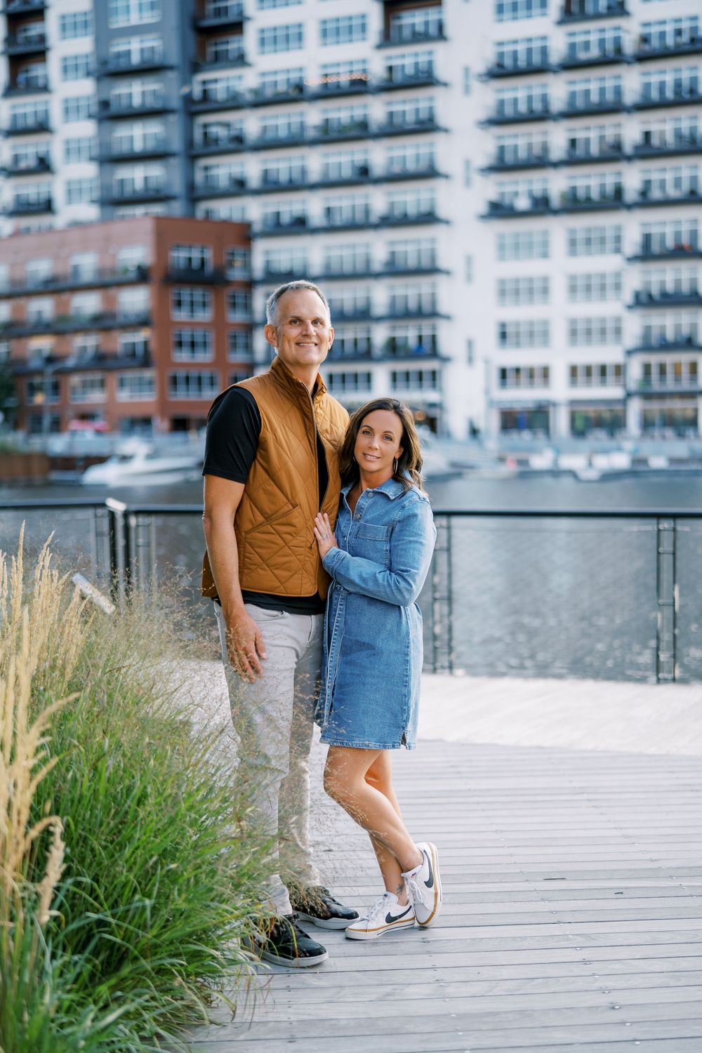 Casual family portraits on wooden boardwalk with modern apartment buildings in background.
