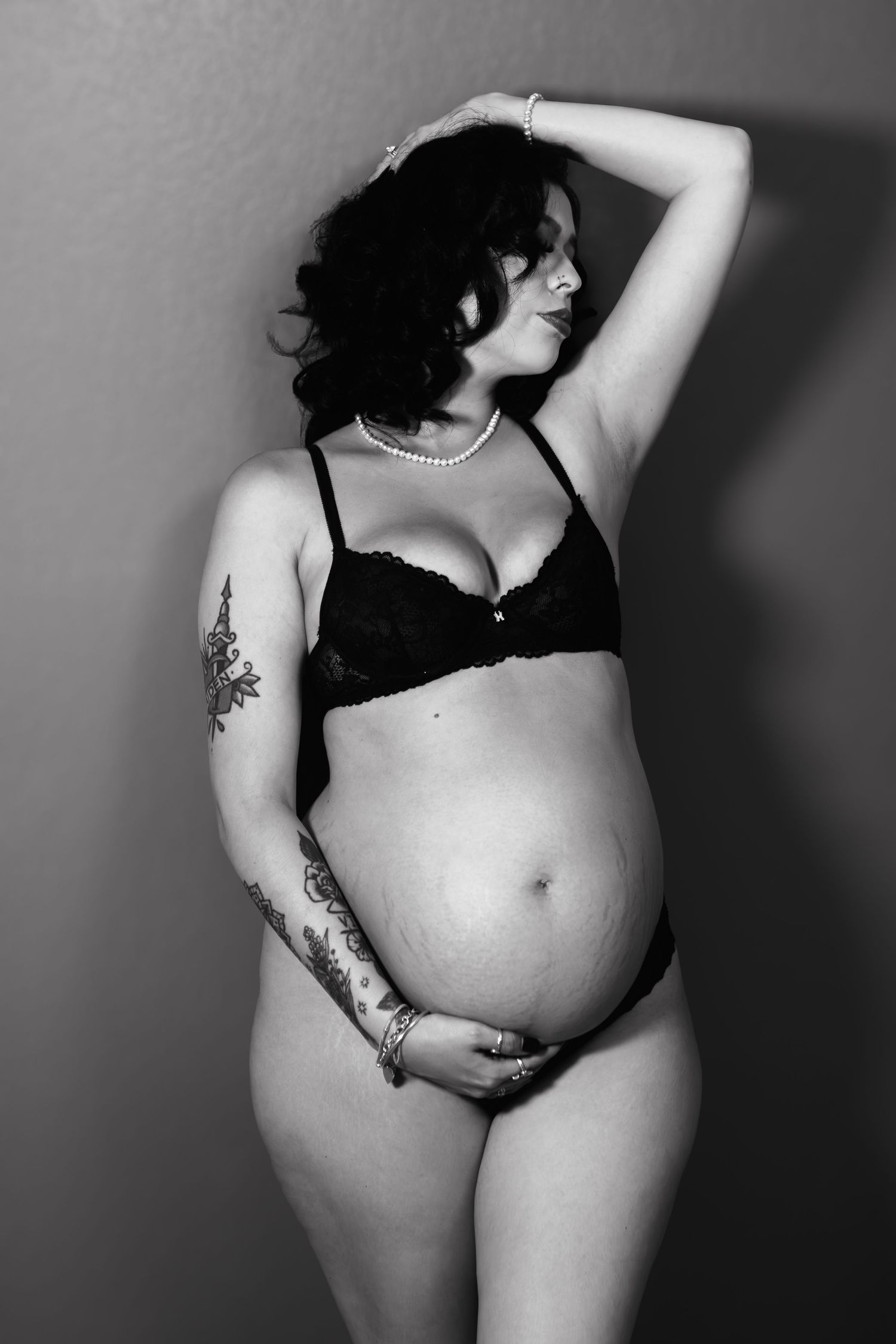 During a boudoir pregnancy photoshoot, a woman leans against the wall of a Fort Worth boudoir studio, while holding her pregnant belly.