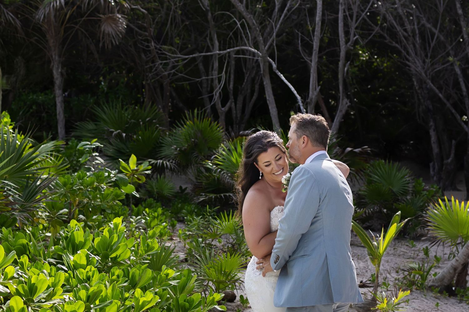 Groom kissing bride in lush greenery at Grand Palladium Kantenah.