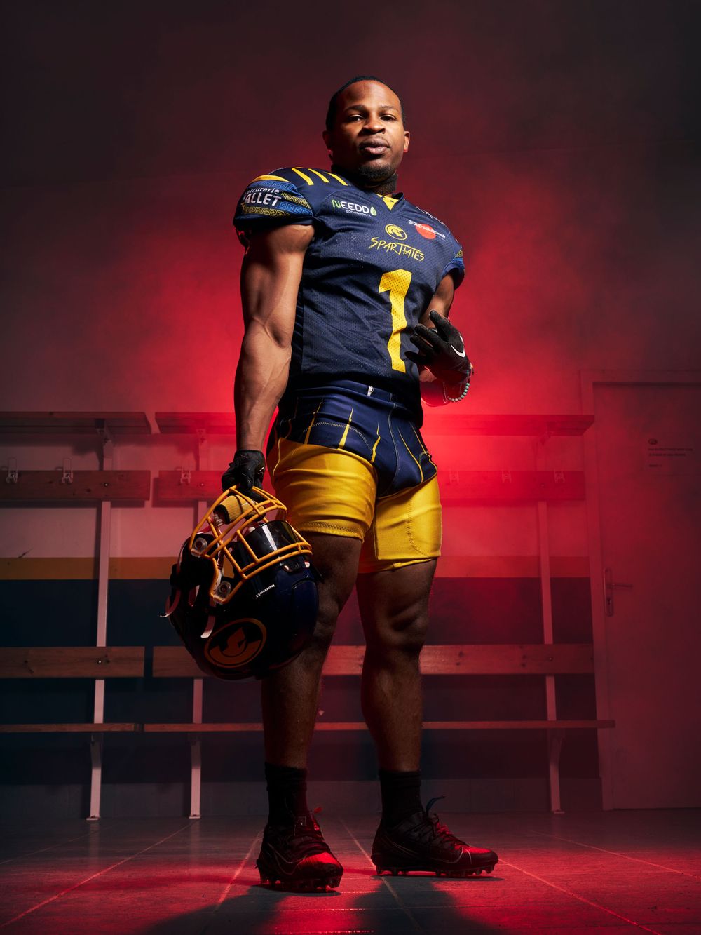 Un joueur de football en uniforme bleu marine et jaune pose de façon spectaculaire avec des effets de lumière rouge.