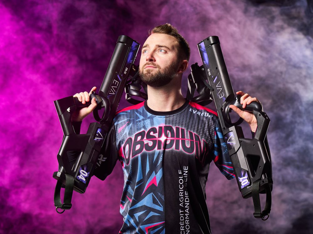 Un joueur compétitif tient des pistolets laser contre la fumée et le brouillard roses colorés tout en portant un maillot d'équipe.