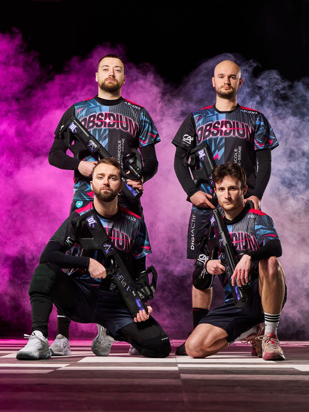 Équipe sportive posant pour une photo dramatique avec des effets de fumée violette et blanche dans des uniformes noirs assortis.