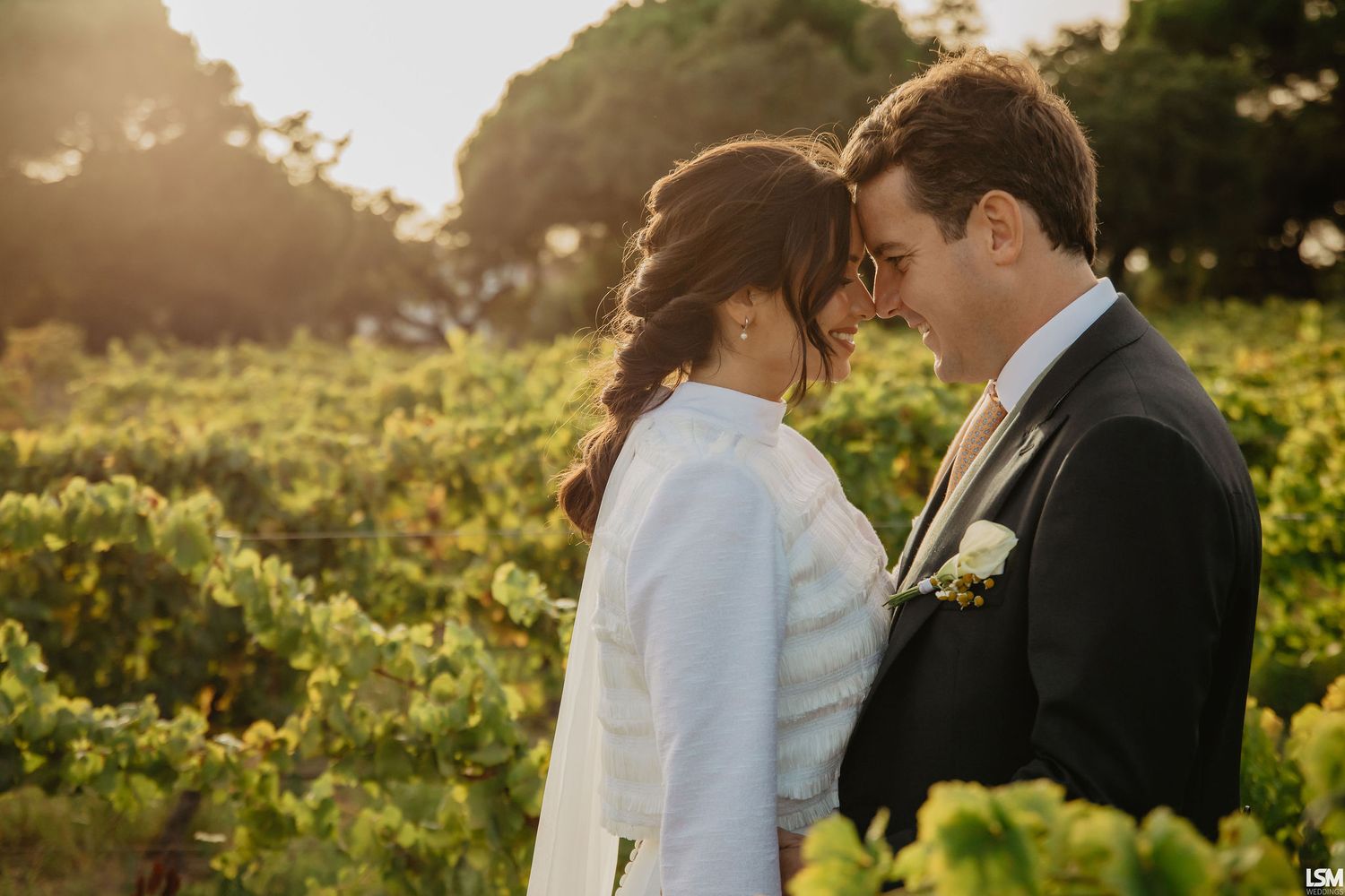 Bride and groom walk hand in hand outdoors at golden hour, bride holding colorful bouquet in elegant white gown.