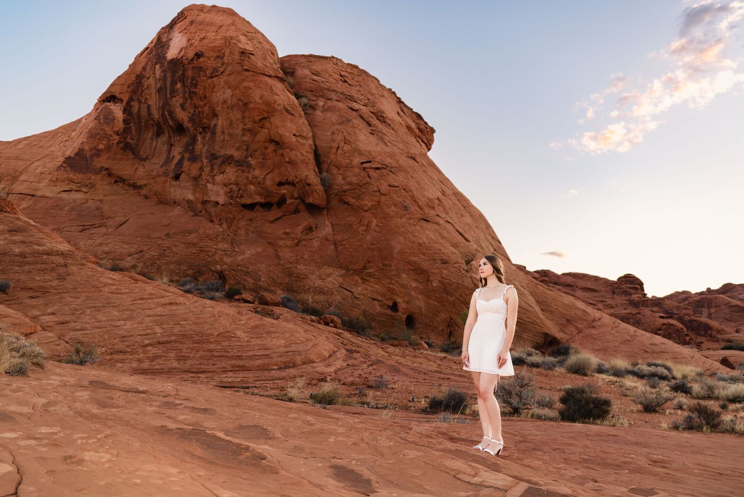 Woman in white dress standing among red rock formations in a desert landscape at Valley of Fire State Park.