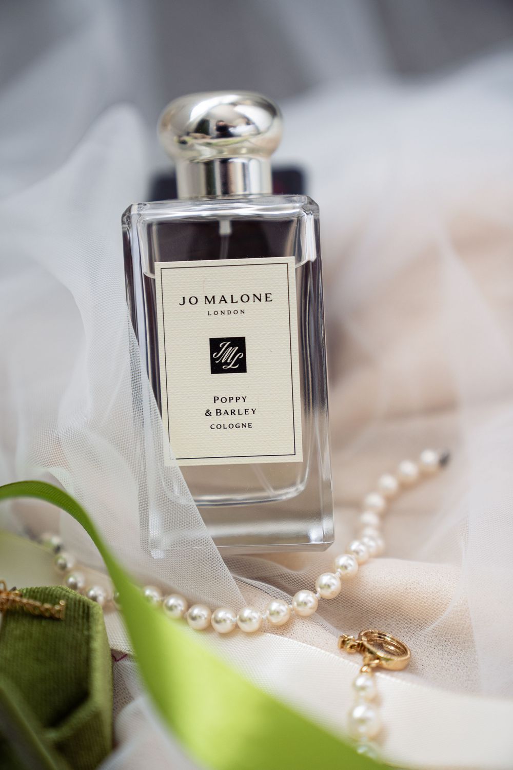 Jo Malone London Poppy & Barley cologne bottle with pearl necklace and green ribbon on soft fabric.