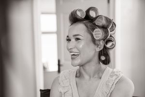 Black and white photo of a smiling bride with hair rollers getting ready for her wedding day.