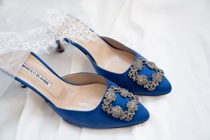 Blue Manolo Blahnik bridal heels with crystal buckle detail resting on white wedding veil.