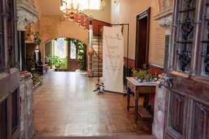 Elegant historic building interior with terracotta floors, stone staircase, and decorative banner in a sunlit hallway.