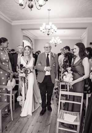 Bride walks down the aisle with her father in a black and white wedding ceremony photo.
