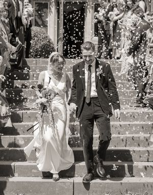 Black and white photo of a bride and groom descending steps in a confetti shower at their wedding ceremony.