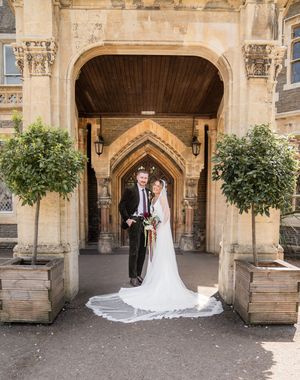 Bride and groom stand beneath a Gothic stone archway flanked by topiary trees at their wedding venue.