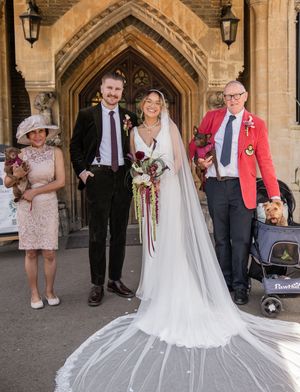 Bride and groom pose with family and dogs outside historic church after wedding ceremony.