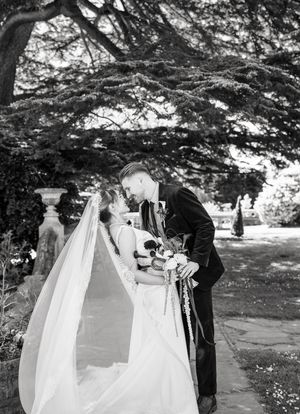 Bride and groom sharing romantic kiss outdoors under trees, stunning black and white wedding portrait.
