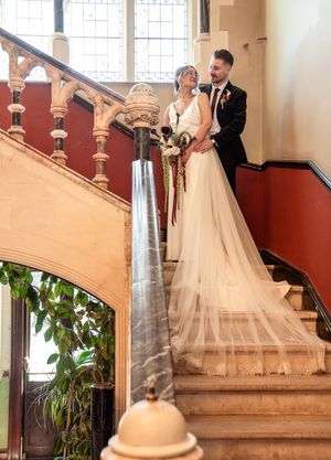 Bride and groom pose on grand staircase in elegant wedding portrait with flowing veil.