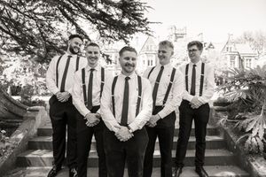 Groom and groomsmen in white shirts and suspenders posing on stone steps, black and white photo.