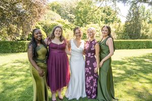 Bride in white gown poses with four bridesmaids in green, purple, and floral dresses outdoors.