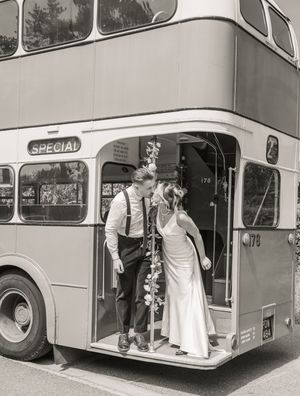 Bride and groom sharing a kiss on a vintage double-decker special bus in black and white wedding photo.